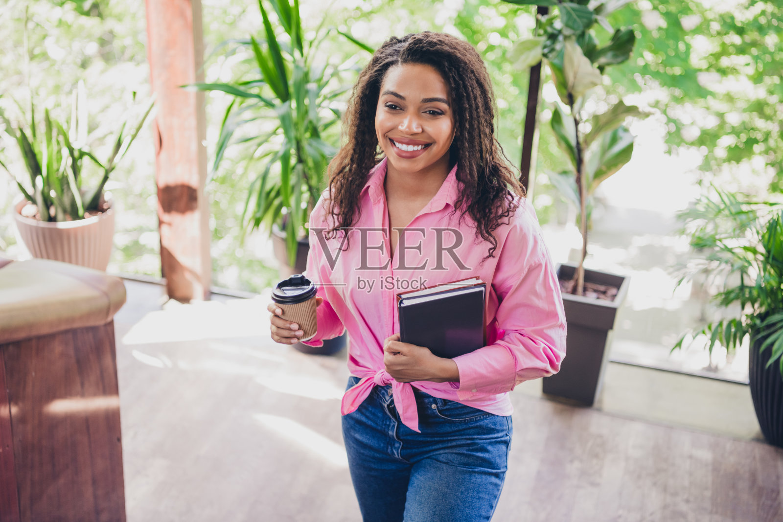 漂亮年轻女孩手持笔记本和咖啡纸杯，穿着粉色衬衫，在共享办公大楼中，成功的初创公司员工。照片摄影图片