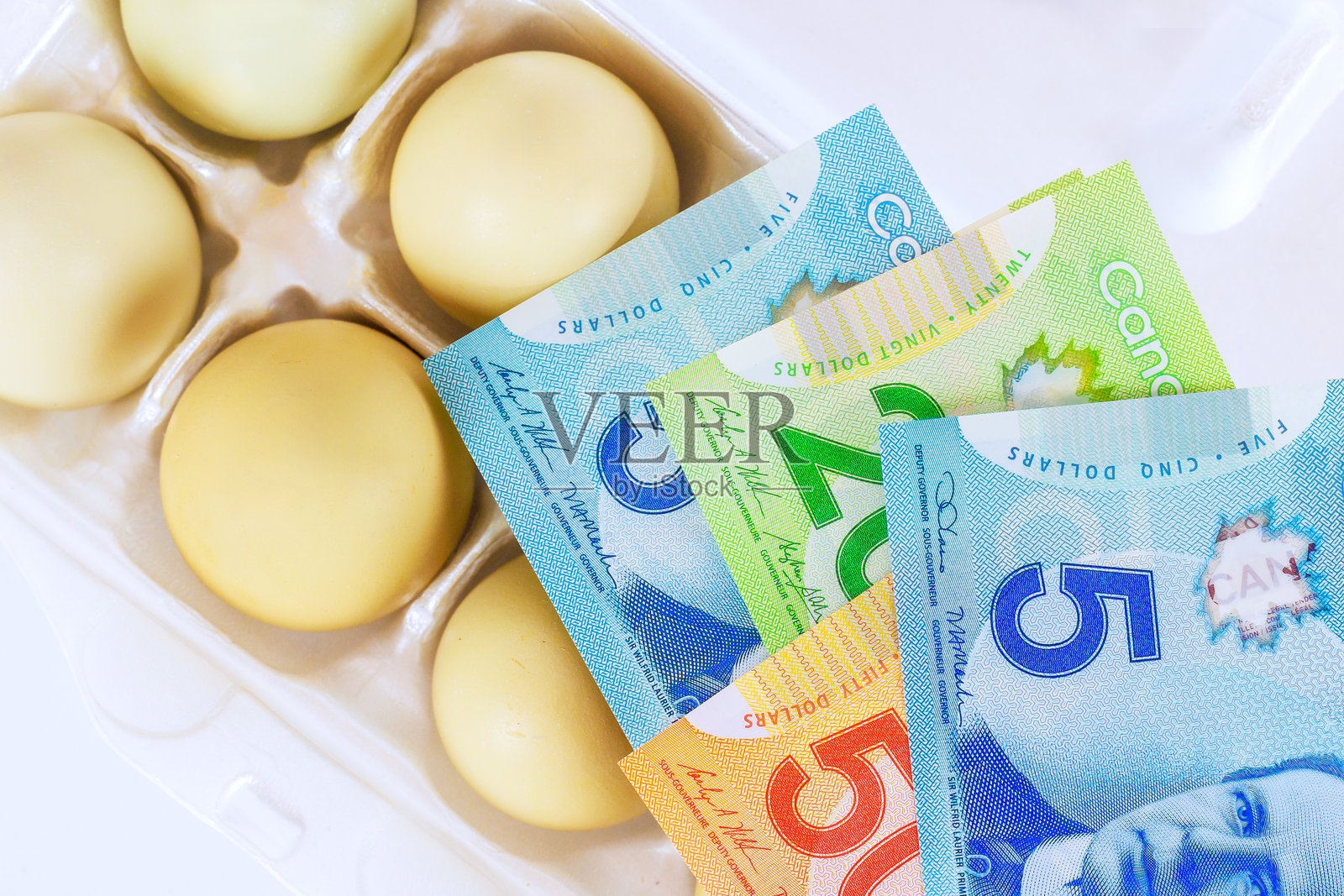 纸箱鸡蛋放在一叠加元钞票旁，突显日常开支的价值，因为鸡蛋价格上涨。照片摄影图片