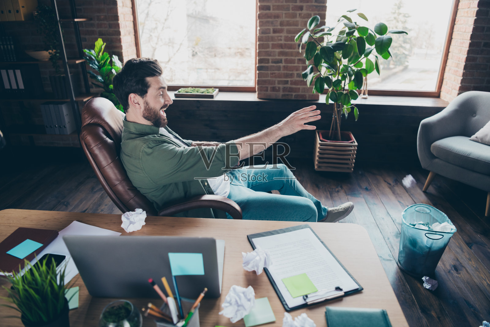 全身照，帅气的年轻男孩在初创公司办公室阁楼内玩耍，把揉成团的纸扔进垃圾桶，穿着绿色衬衫。照片摄影图片