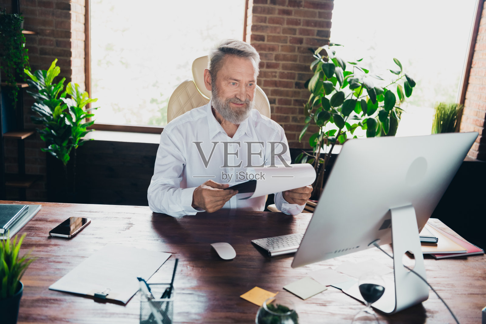 成功的男性房地产专家穿着衬衫，在室内工作站阅读文件报告合同照片摄影图片