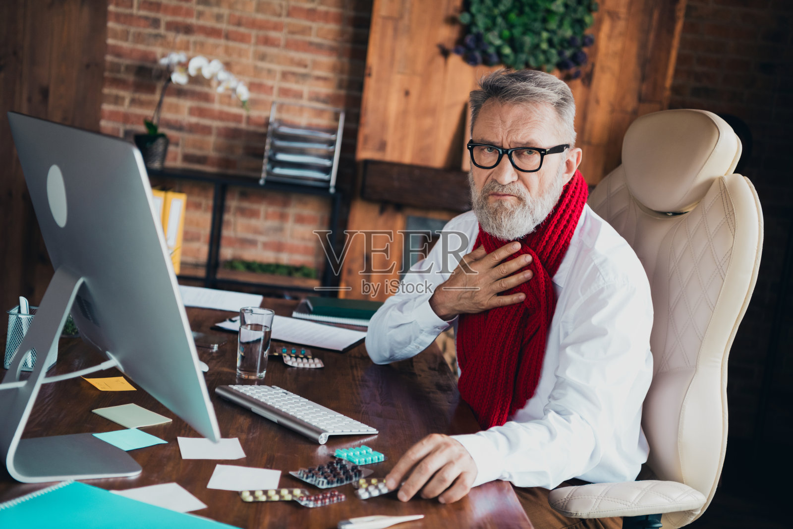 穿着白色衬衫的和蔼老人在明亮的办公室里服用药片，喉咙痛，展现出成功的职场形象。照片摄影图片