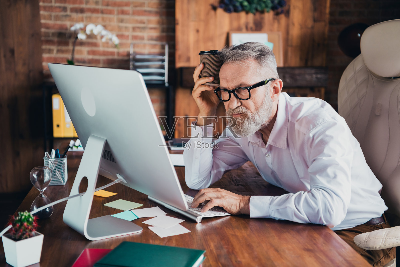 疲惫的退休男士，身穿白衬衫，低能量的早晨，坐在室内工作站或车间。照片摄影图片