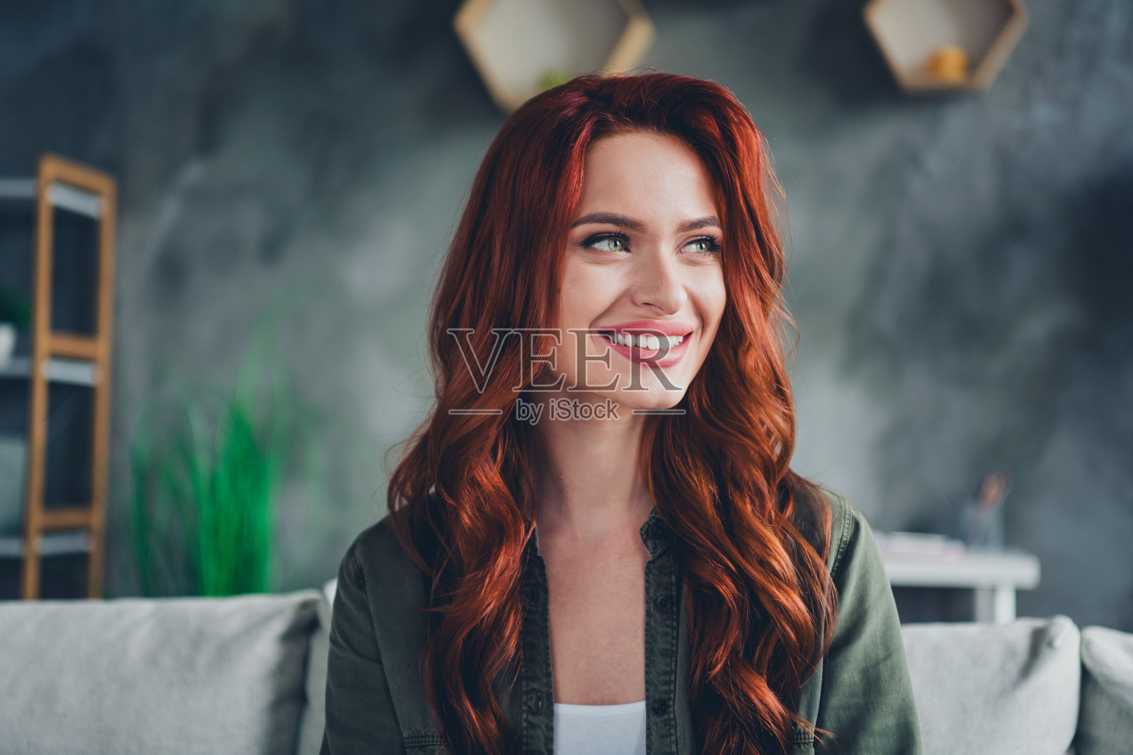 穿着绿色衬衫的漂亮快乐女士在室内沙发上微笑放松照片摄影图片