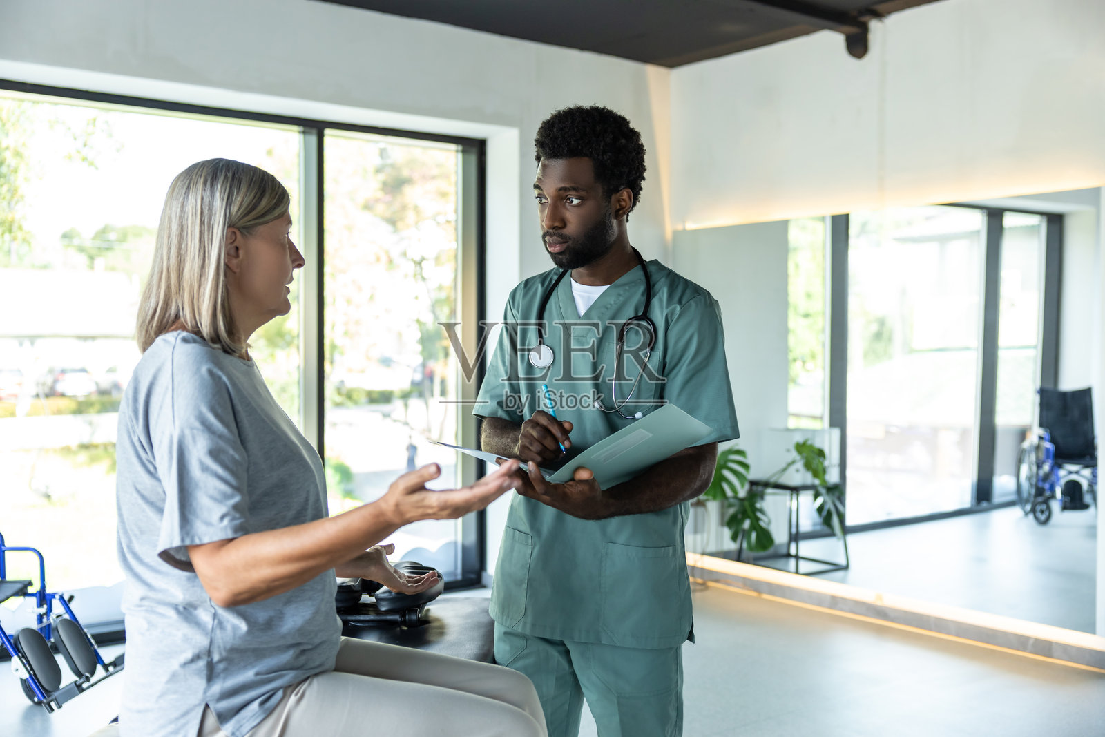 肤色较深的年轻男性医生在康复诊所与女性患者交谈照片摄影图片