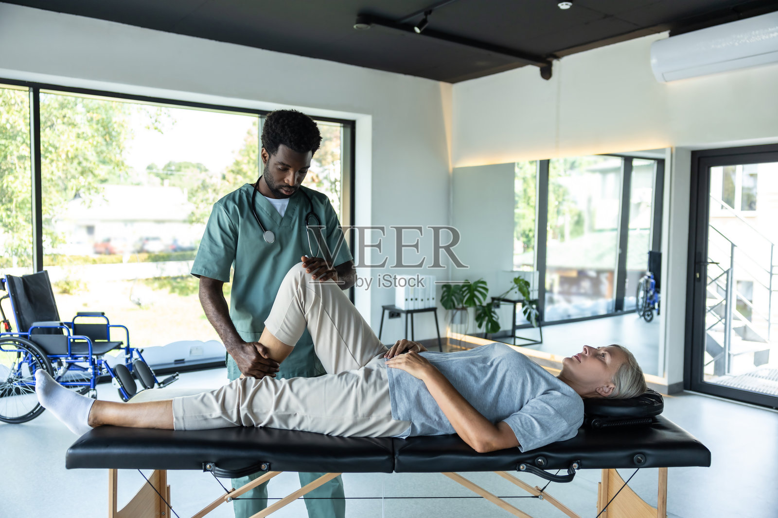 女性病人躺在沙发上，男性医生正在为她的腿进行拉伸。照片摄影图片