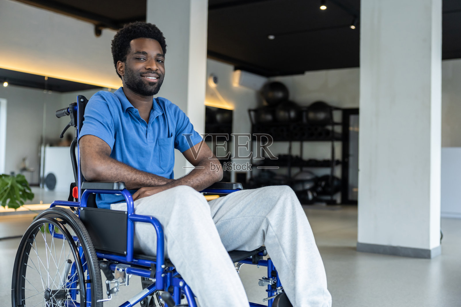 微笑的年轻非裔美国男子坐在轮椅中，位于诊所走廊。照片摄影图片