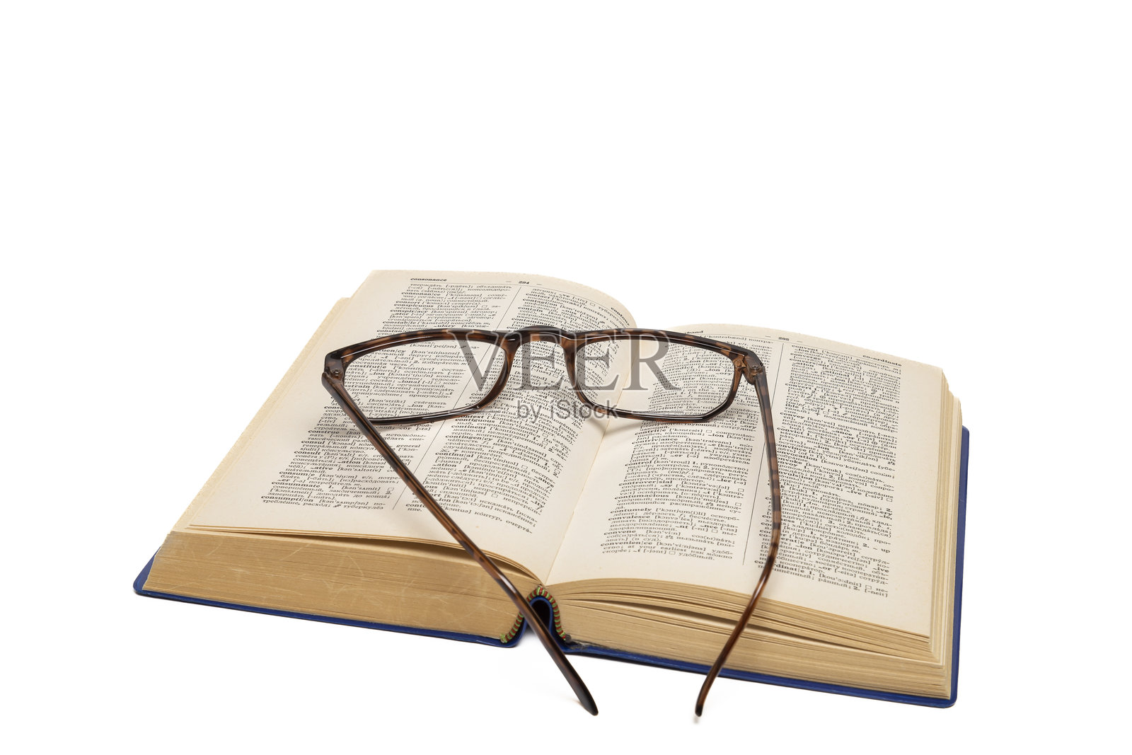 一本旧的打开的字典，上面放着一副眼镜，背景为白色。照片摄影图片