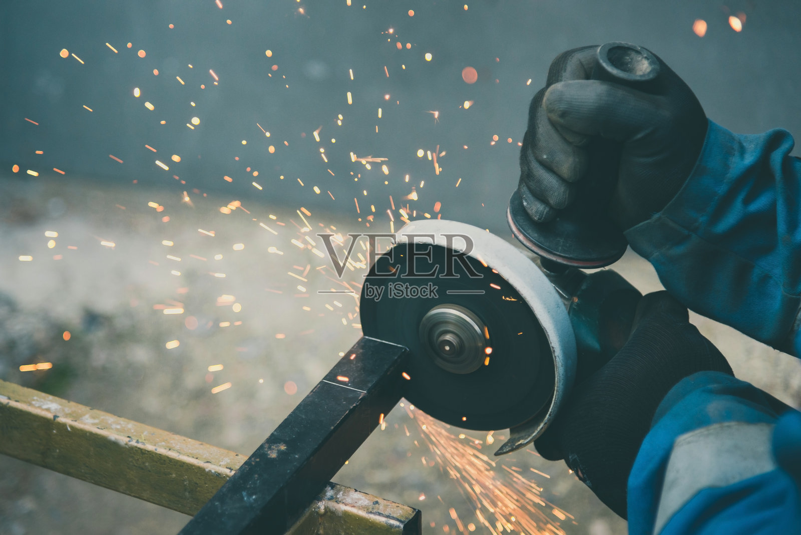 戴着安全手套的男子正在用手持磨光机切割金属，产生大量火花。照片摄影图片