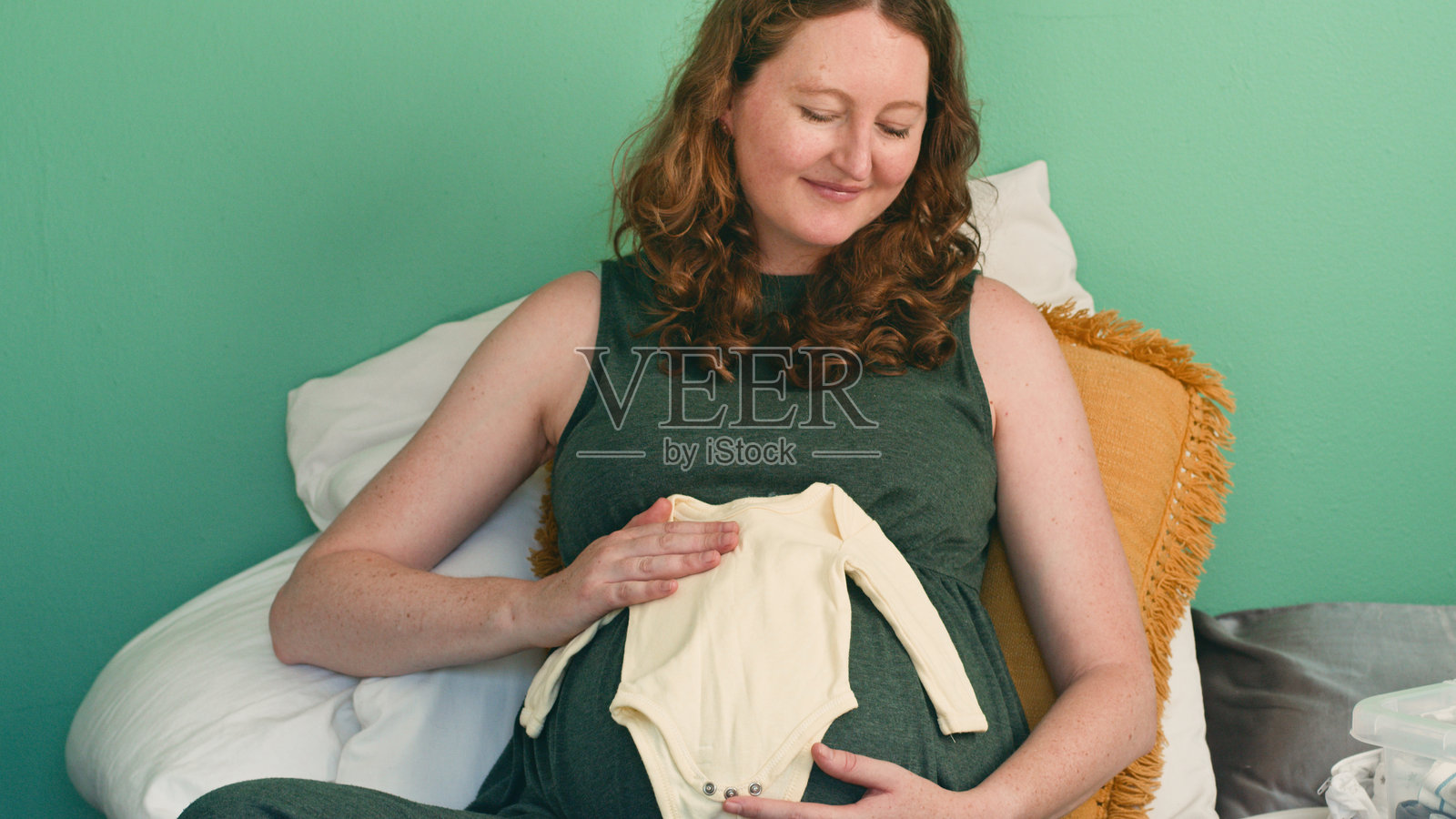 快乐的孕妇在家中享受宁静时光，肚子上放着婴儿衣服照片摄影图片