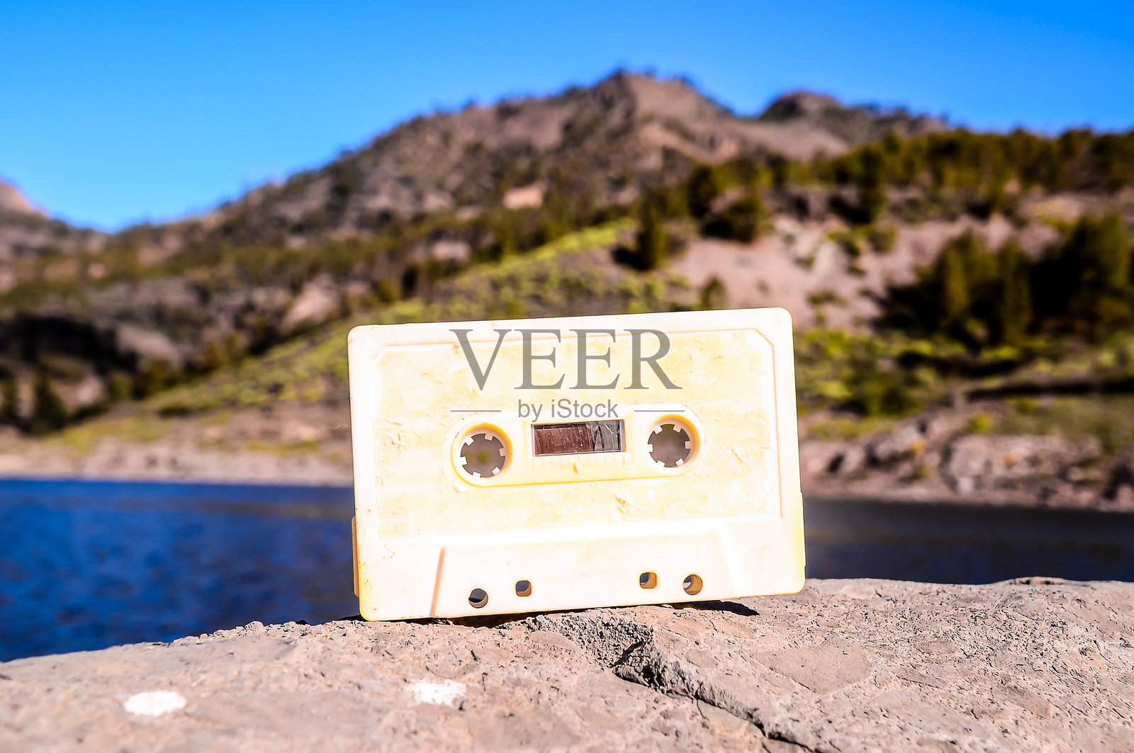 一盘黄色的卡带放在水边的一块石头上照片摄影图片