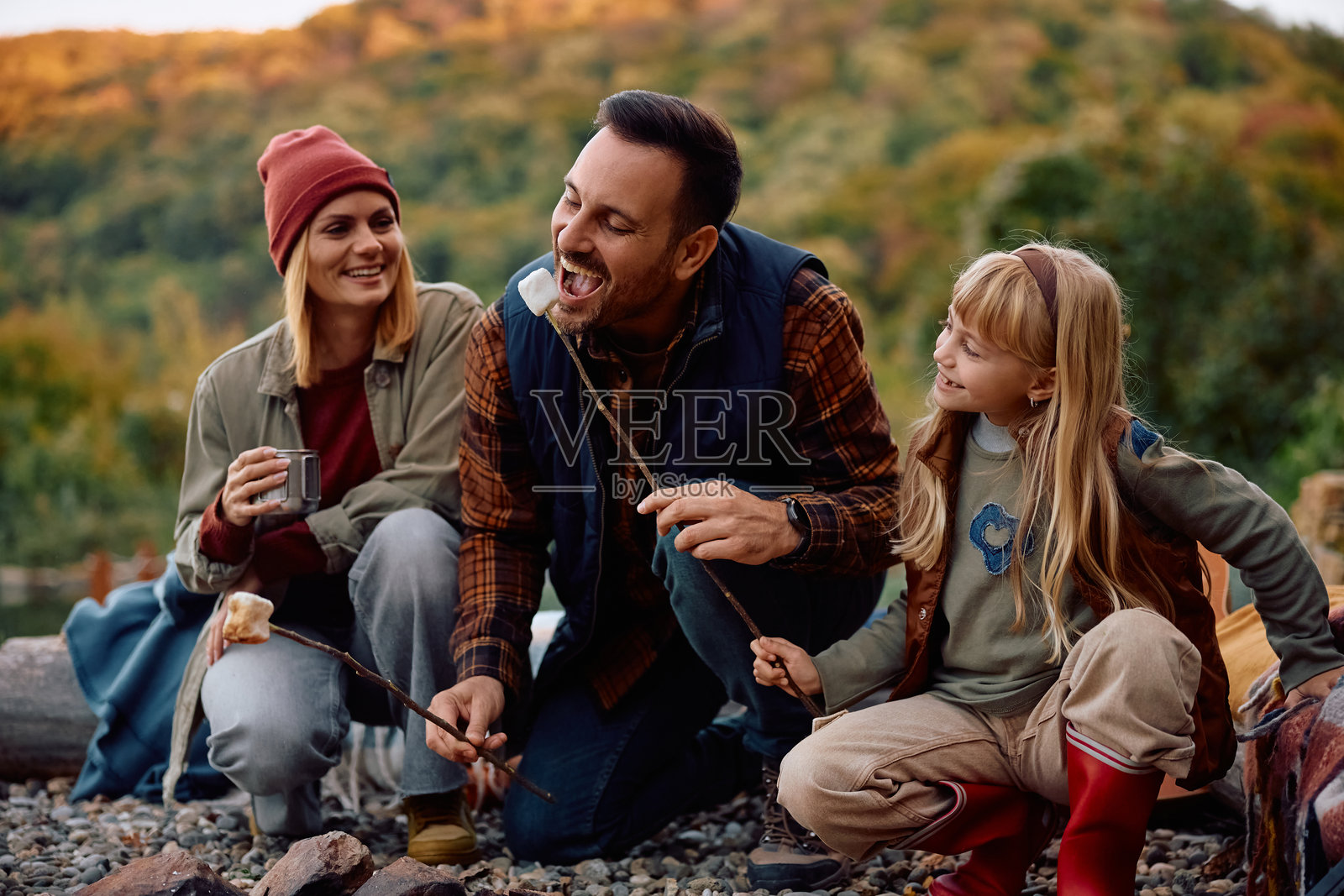 快乐的家庭在篝火旁烤棉花糖，享受欢乐时光。照片摄影图片