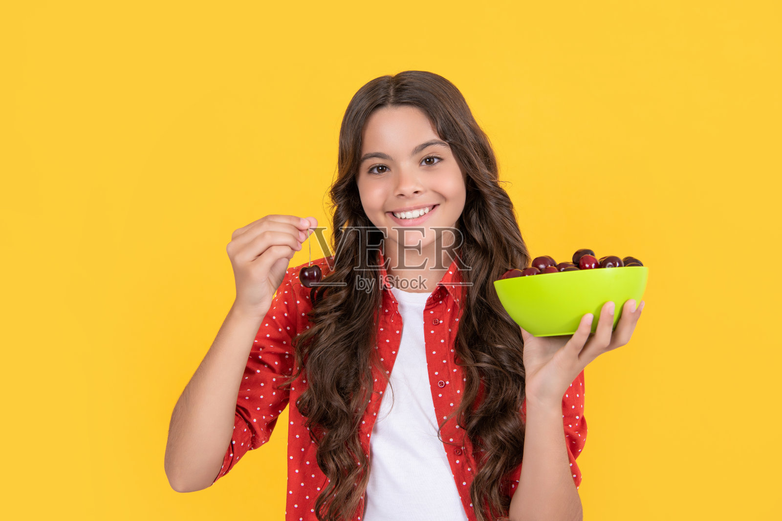 快乐的少女在黄色背景下举着樱桃碗照片摄影图片