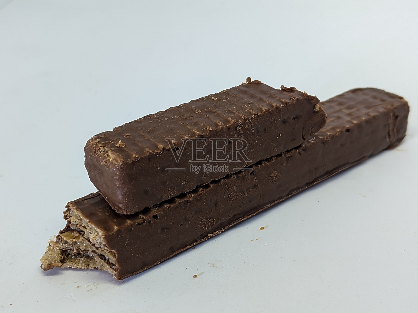 两根巧克力涂层的威化棒叠在一起，其中一根稍微断裂，露出了里面的脆层。照片摄影图片