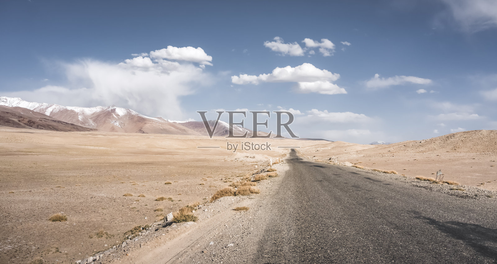 帕米尔公路的沥青道路在塔吉克斯坦的天山山谷中蜿蜒曲折，背景是高沙漠山脉的风景。照片摄影图片