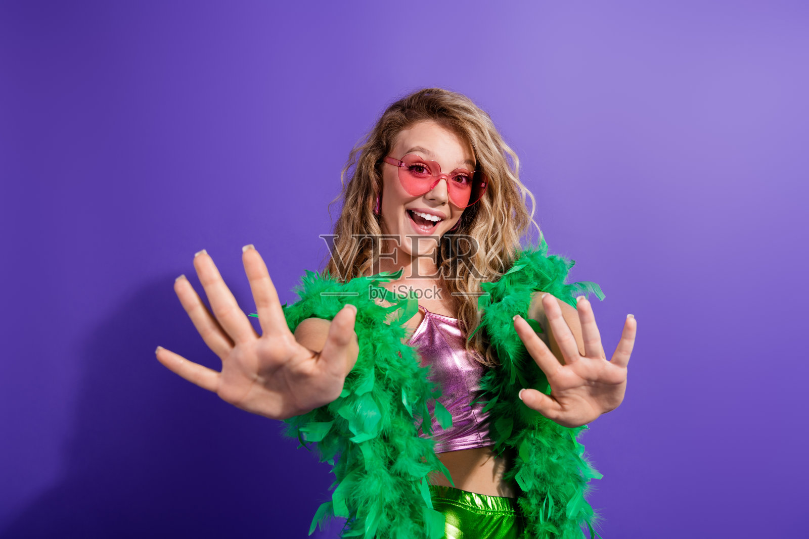 年轻女性穿着时尚闪亮的上衣，搭配绿色羽毛围巾，背景为生动的紫色，散发出快乐与风格。照片摄影图片