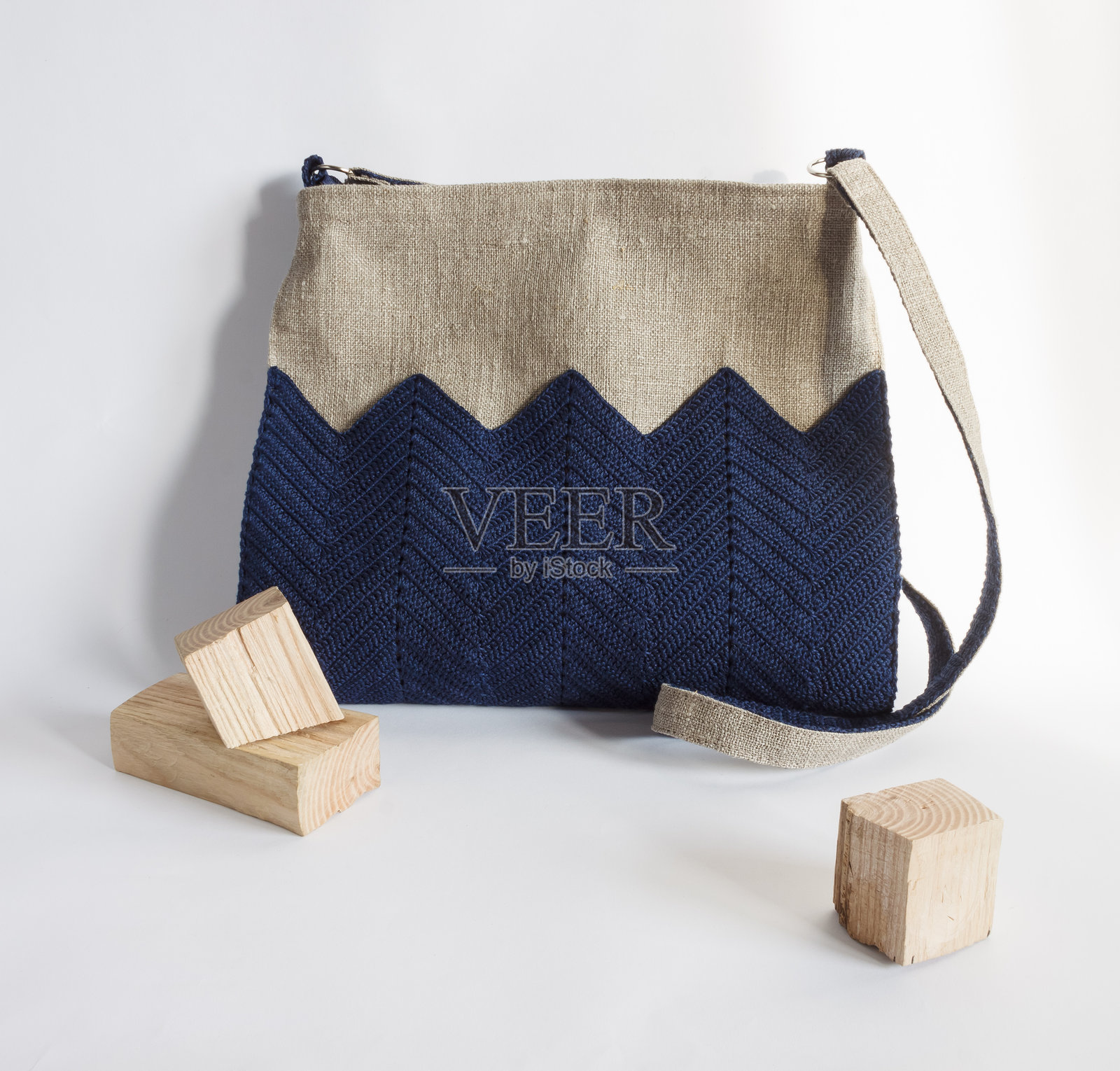 这款斜挎包由亚麻制成，装饰有蓝色针织装饰。背景为浅色。照片摄影图片