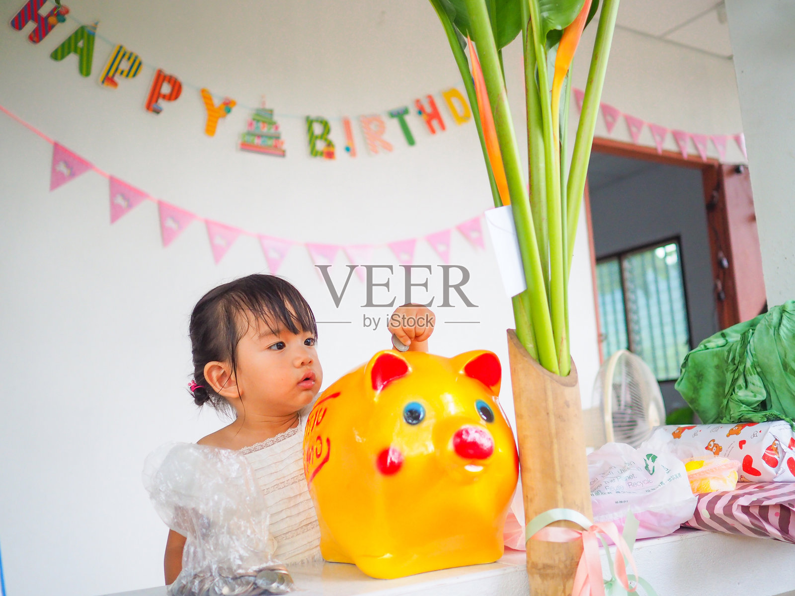 可爱女孩把存钱罐靠在墙上。照片摄影图片