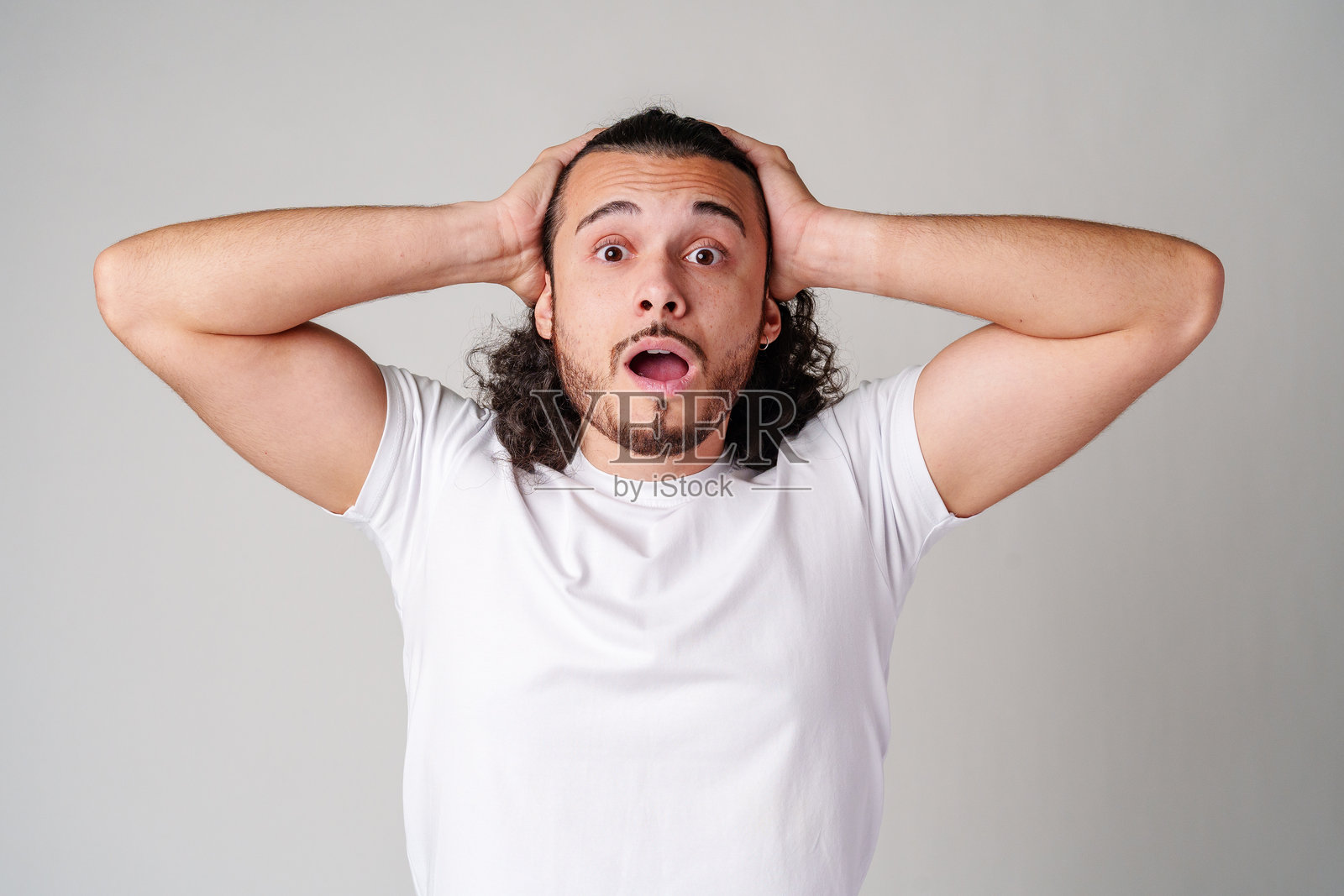 一个卷发男士在中性背景下向上看，露出惊讶的表情照片摄影图片