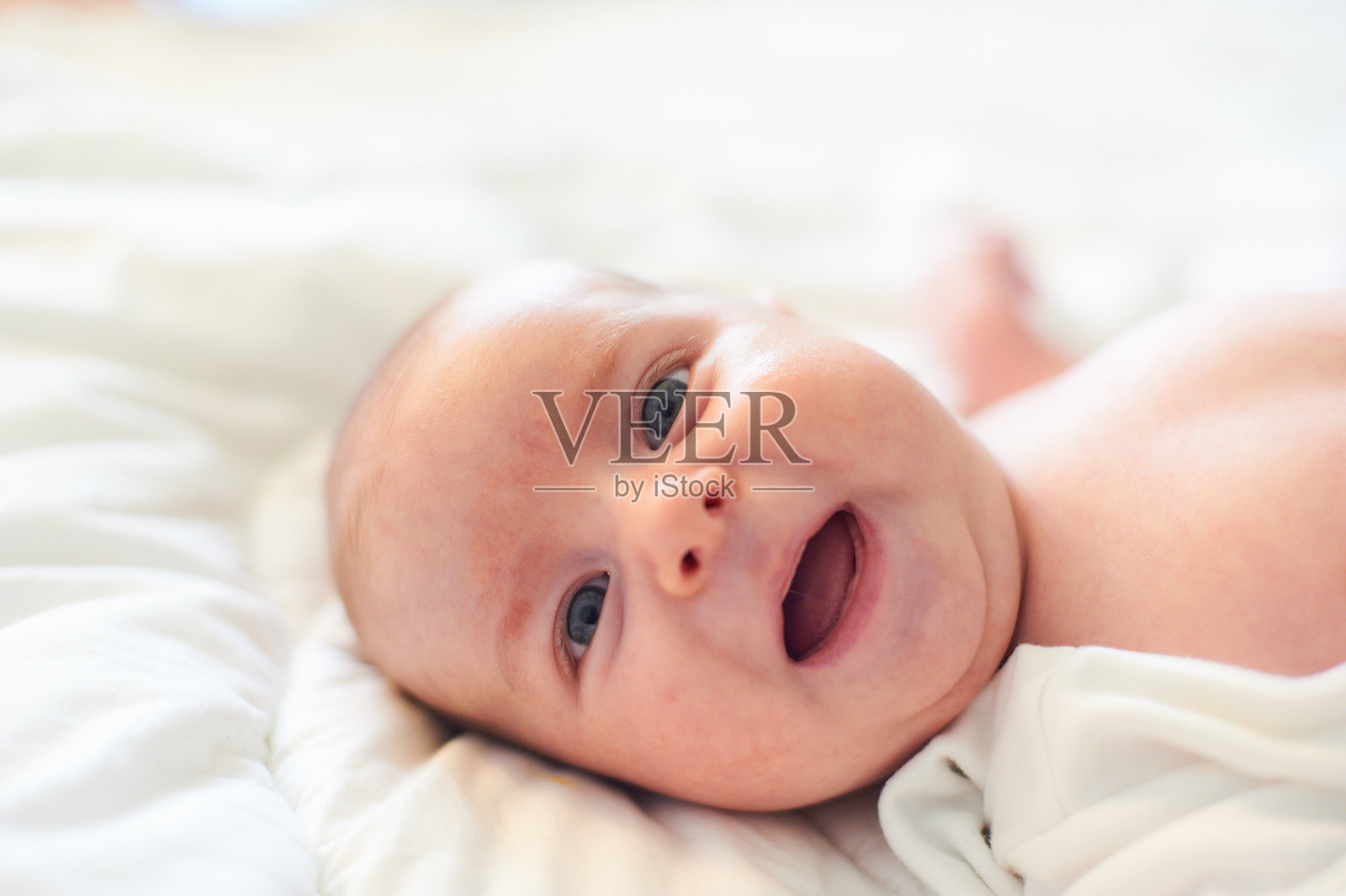 阳光明媚的早晨，快乐的宝宝在柔软的白色床上微笑。照片摄影图片