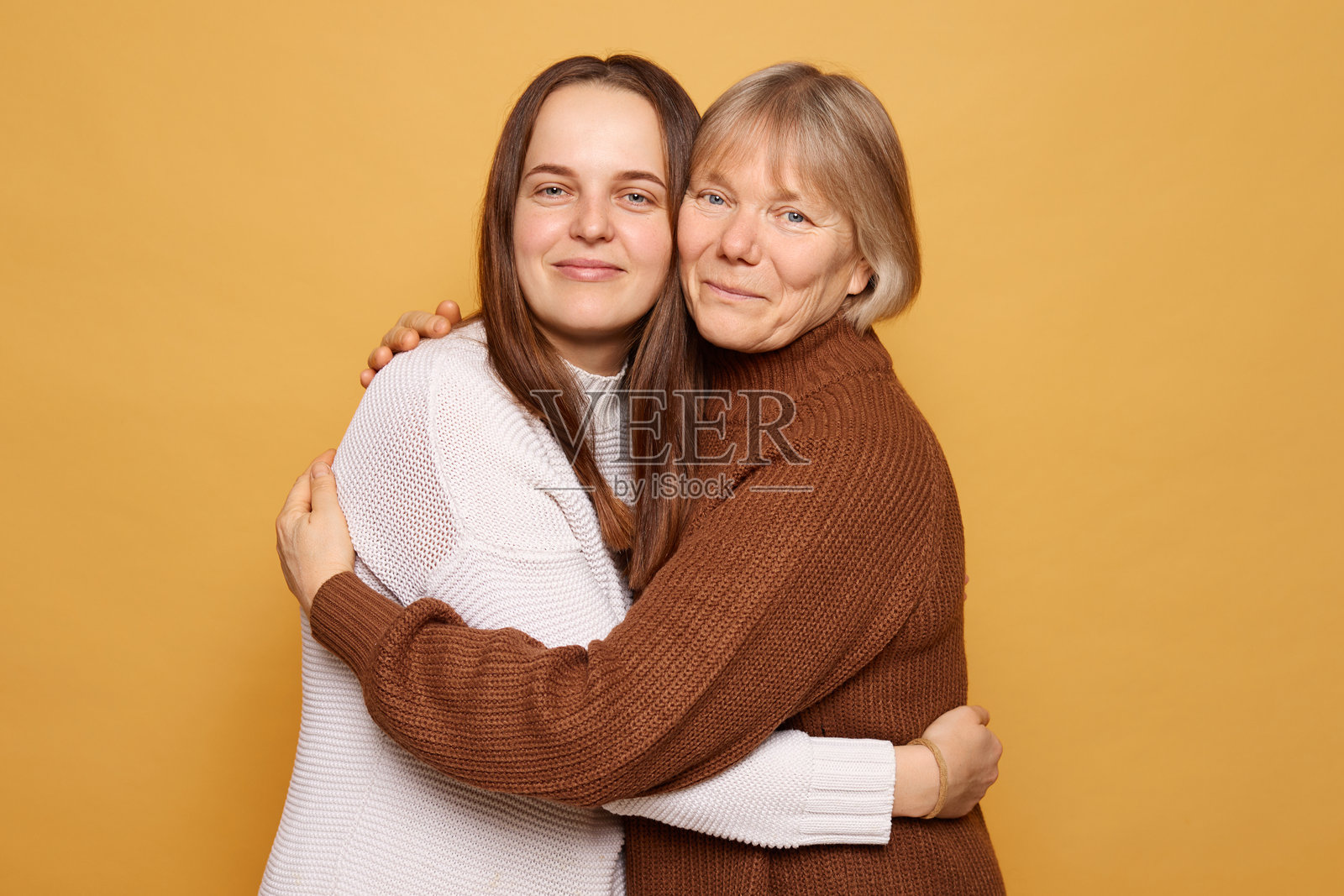 两位女性在鲜艳的黄色背景下温暖相拥，展现了她们在快乐时刻的亲密关系和深厚感情。照片摄影图片
