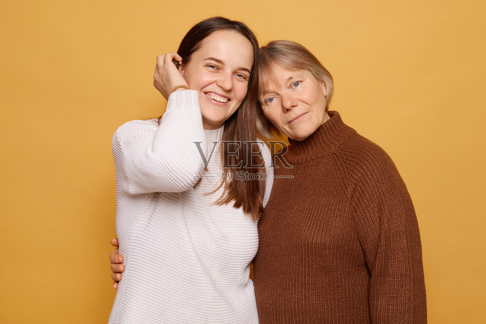 两位女性紧密站在一起，面带温暖的微笑，背景是明亮的黄色，展现了她们在轻松肖像拍摄中愉快的联系和深厚的情感。照片摄影图片
