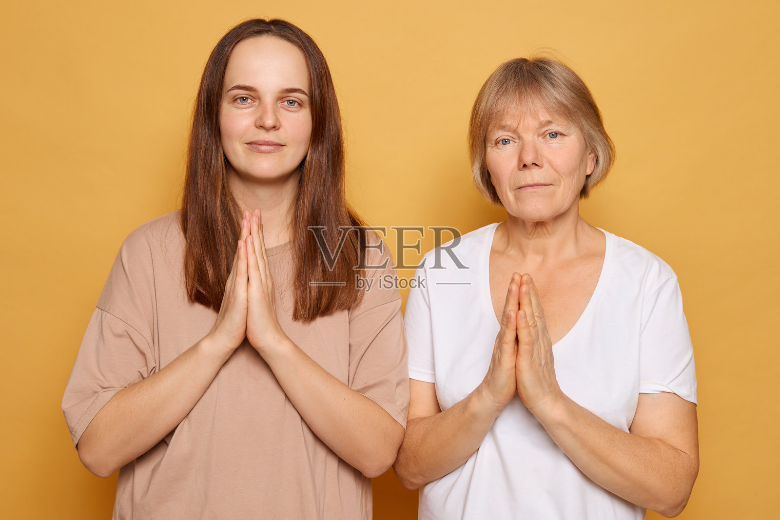两位女性站在一起，双手合十，背景是明亮的黄色，展现出在宁静环境中团结与和平的时刻。照片摄影图片