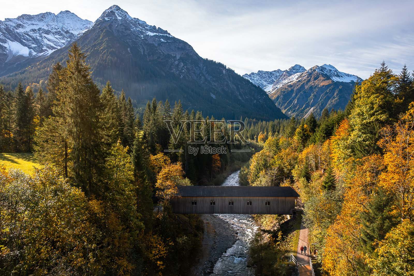 奥地利阿尔卑斯山一对可爱的情侣在野生山河旁漫步，远处是一座有顶桥的鸟瞰图照片摄影图片