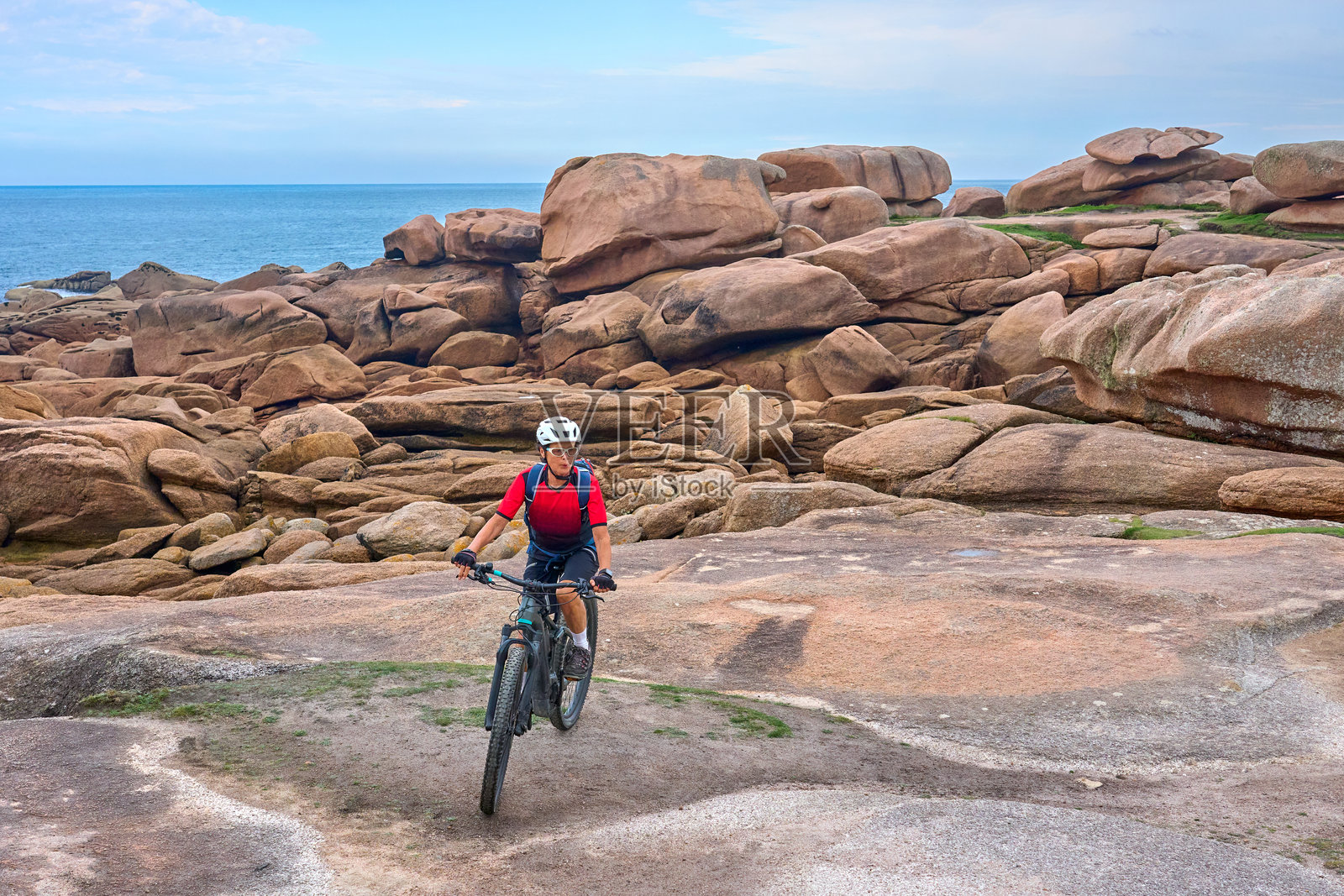 在法国布列塔尼的科特迪阿摩尔，岩石玫瑰花岗岩海岸骑自行车的女性照片摄影图片