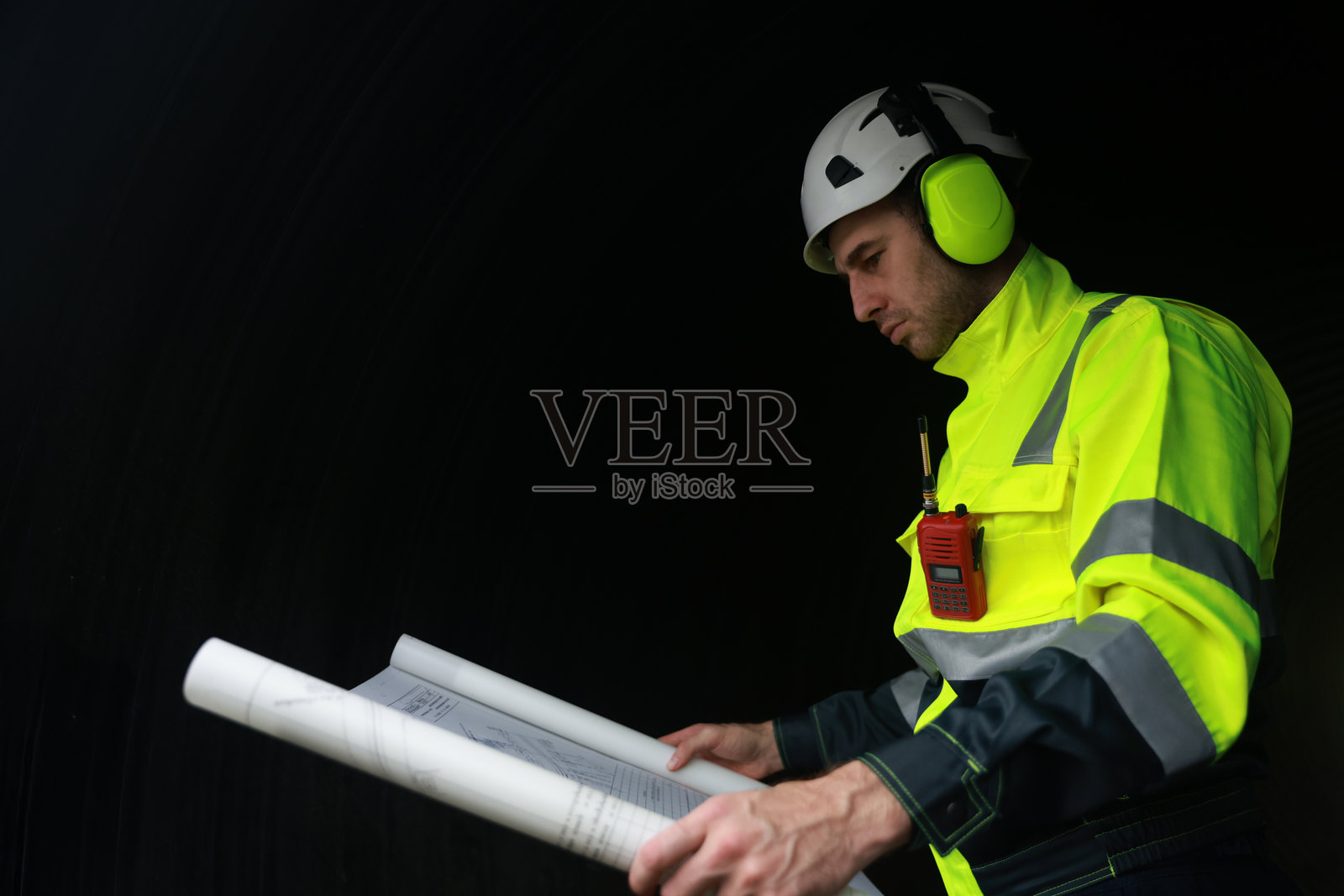 穿着绿色安全夹克和耳罩的聪明工程师在隧道管道中阅读图纸的肖像照片摄影图片