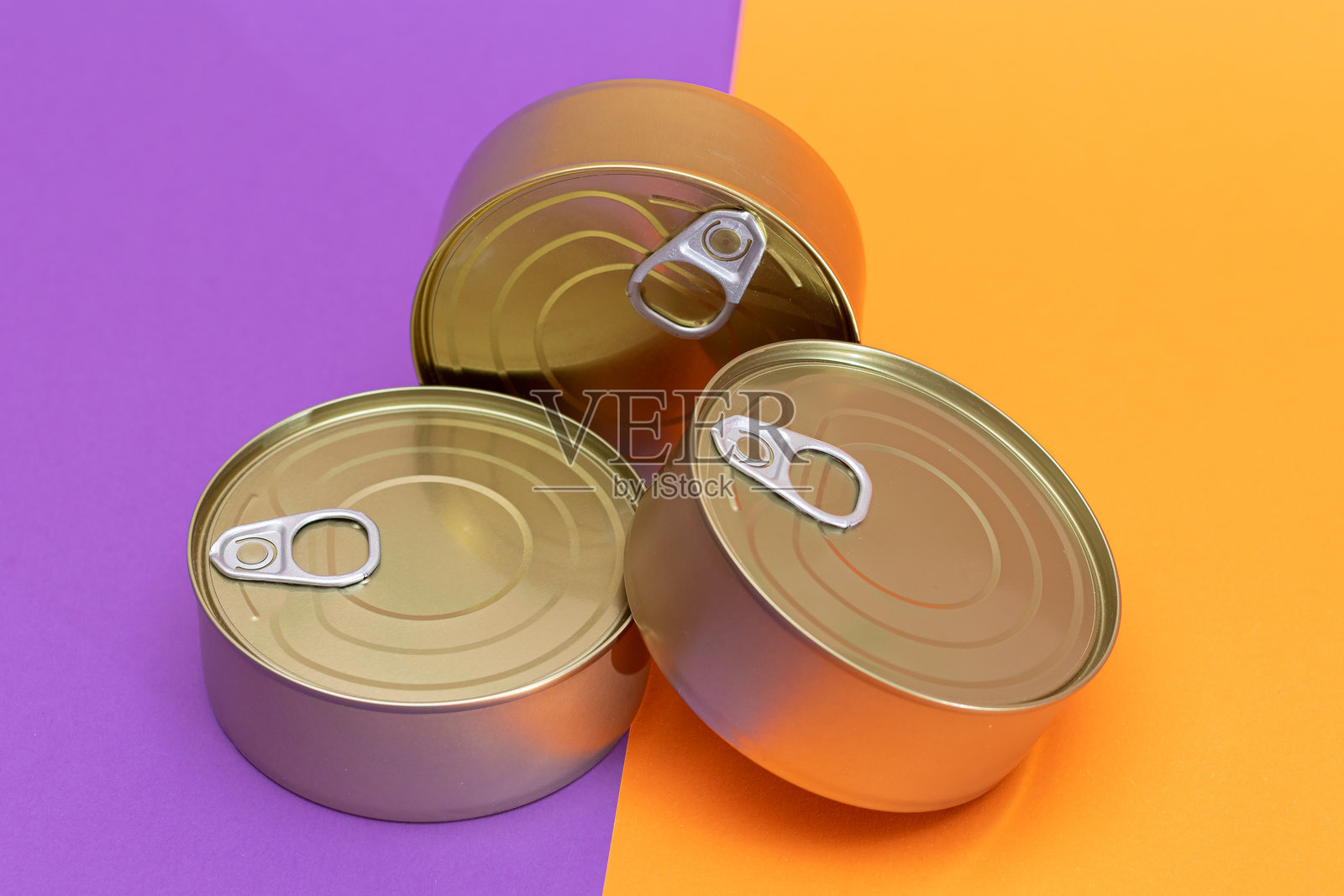 一组叠放的空罐子，边缘空白，背景为分割的橙色和紫色。照片摄影图片