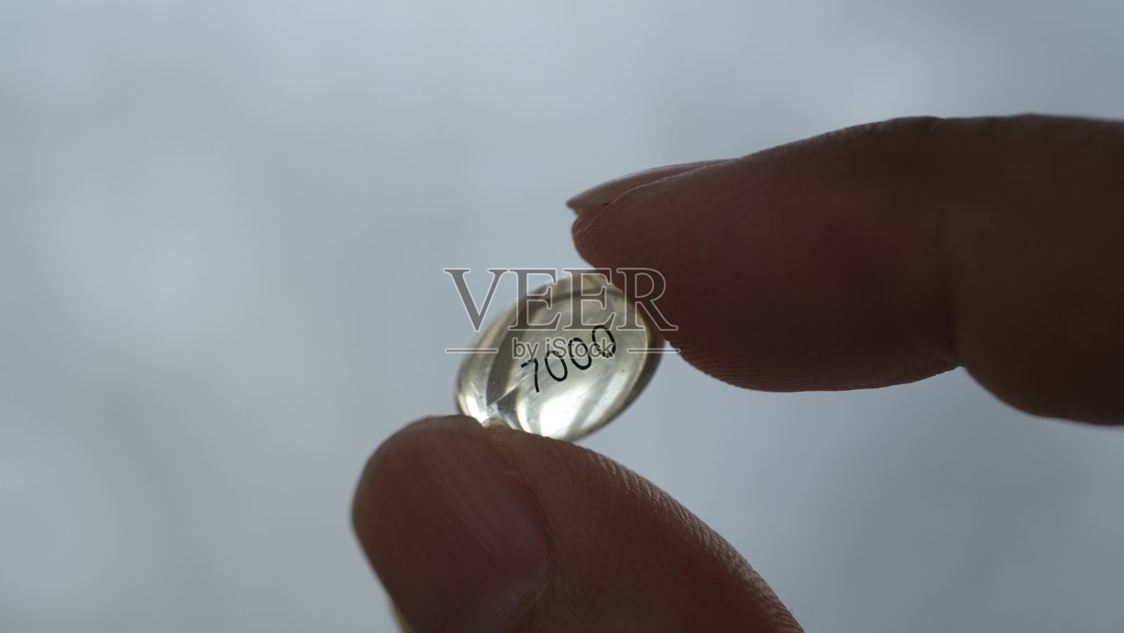 手指握着高剂量7000单位维生素D3软胶囊。照片摄影图片