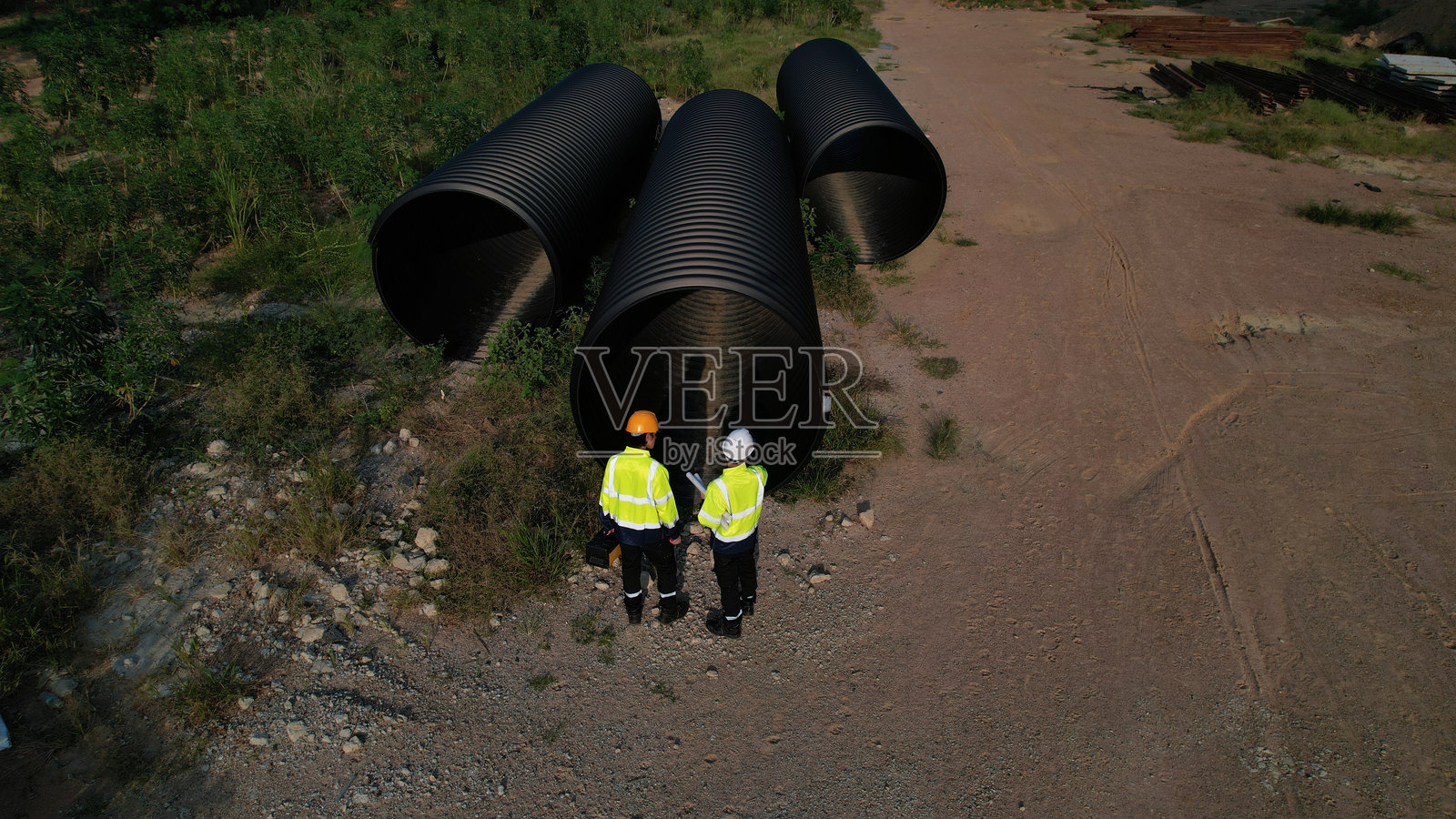 两名年轻的建筑工程师在工地上俯瞰并检查大型排水管材料，准备将其运输到郊区建立新的道路系统。照片摄影图片