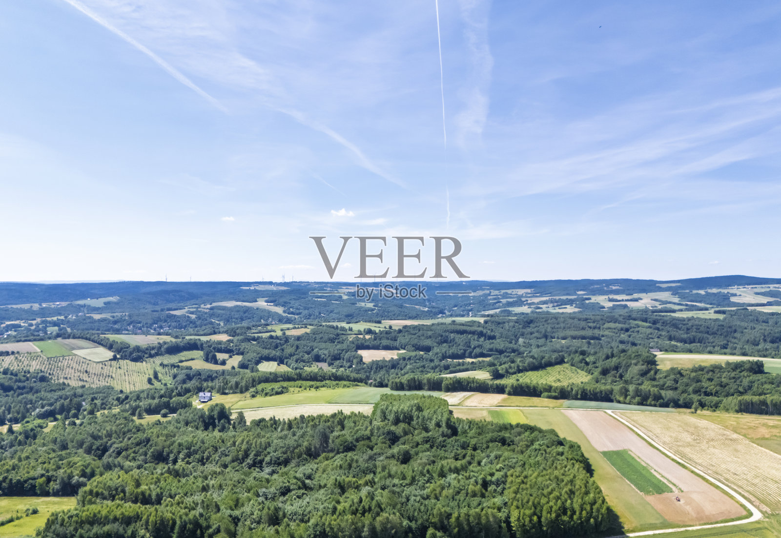 美丽的鸟瞰图，展现了郁郁葱葱的绿色田野和森林，映衬在明亮的蓝天之下，展示了自然与农业的和谐。照片摄影图片