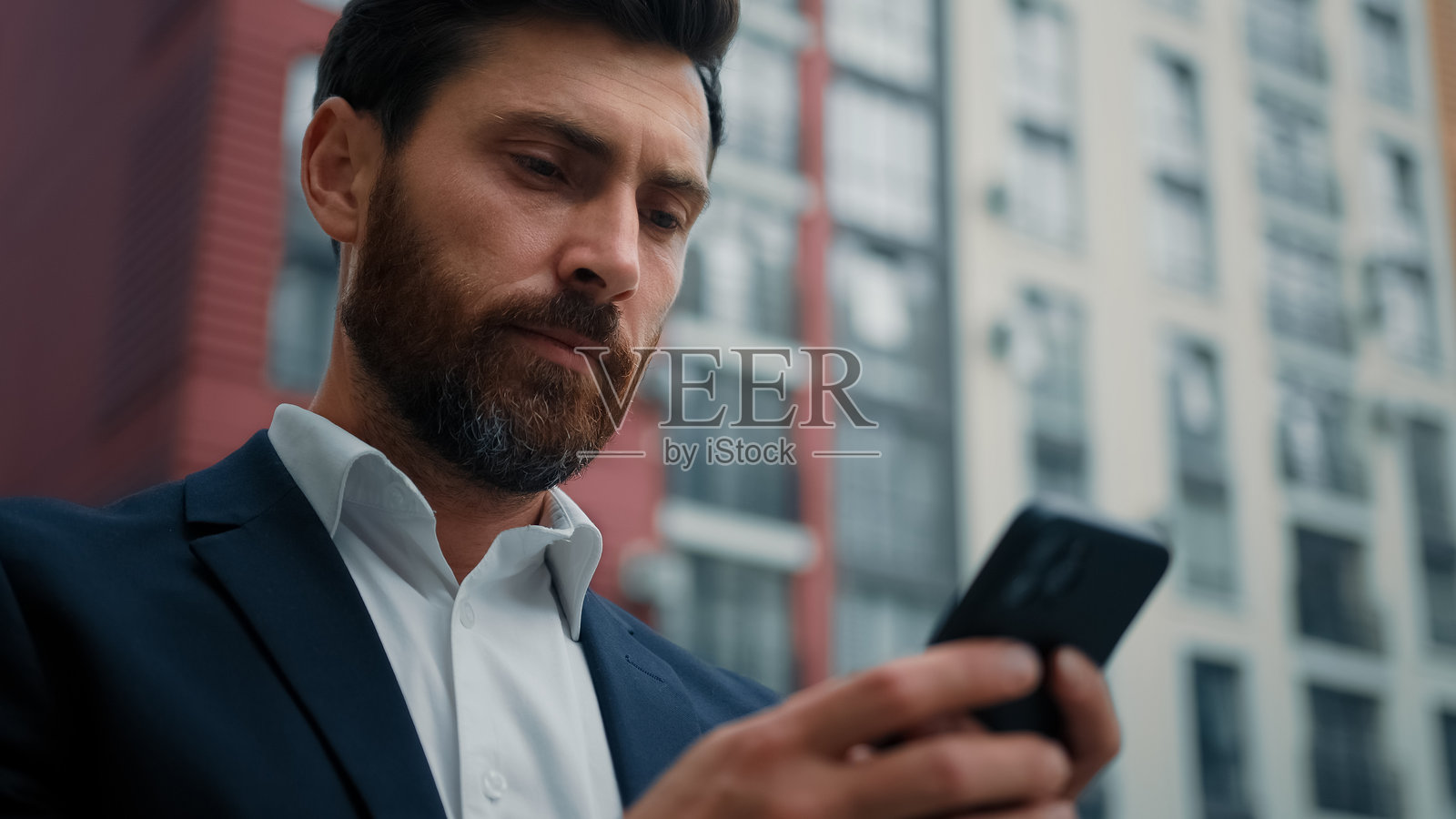 男性商人在手机上发送信息，在线聊天，搜索信息，查看通知，30多岁的白人男性自由职业者，在城市中使用现代智能手机浏览互联网，使用WiFi。照片摄影图片