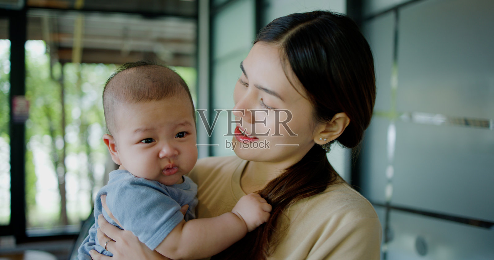 一位年轻女性在咖啡店里抱着一个哭泣的小男孩。照片摄影图片