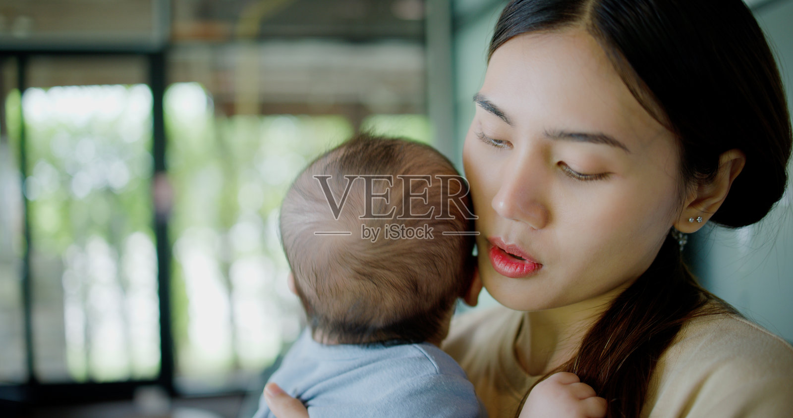 一位年轻女性在咖啡店里抱着一个哭泣的小男孩。照片摄影图片