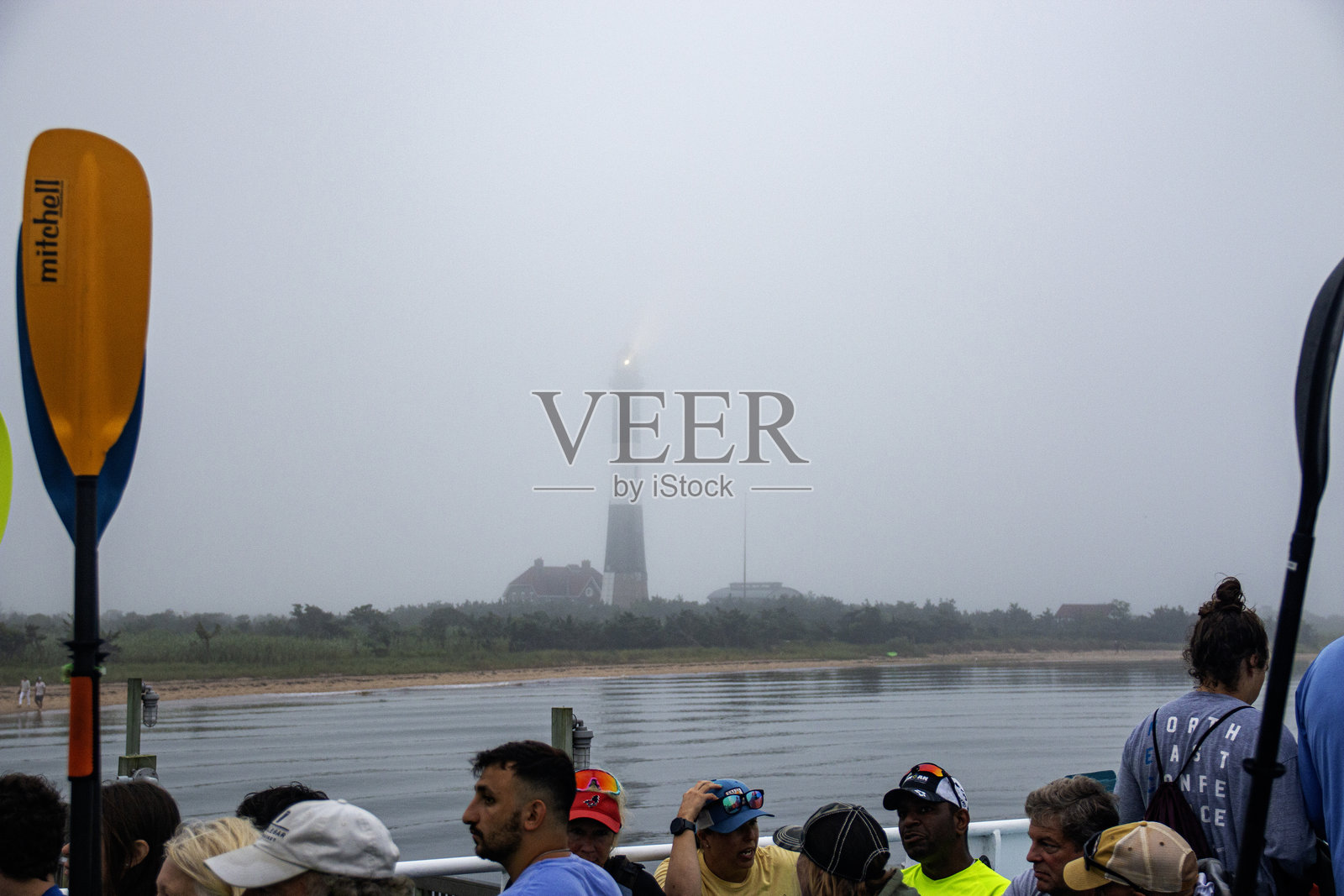 雾蒙蒙的海滩上,一群人靠近远处的灯塔。照片摄影图片