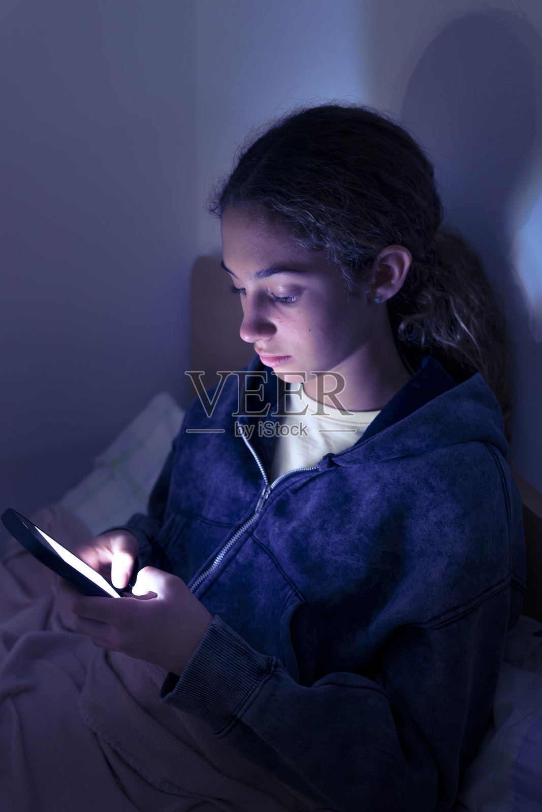 青少年女孩深夜躺在床上使用智能手机。儿童屏幕成瘾。照片摄影图片