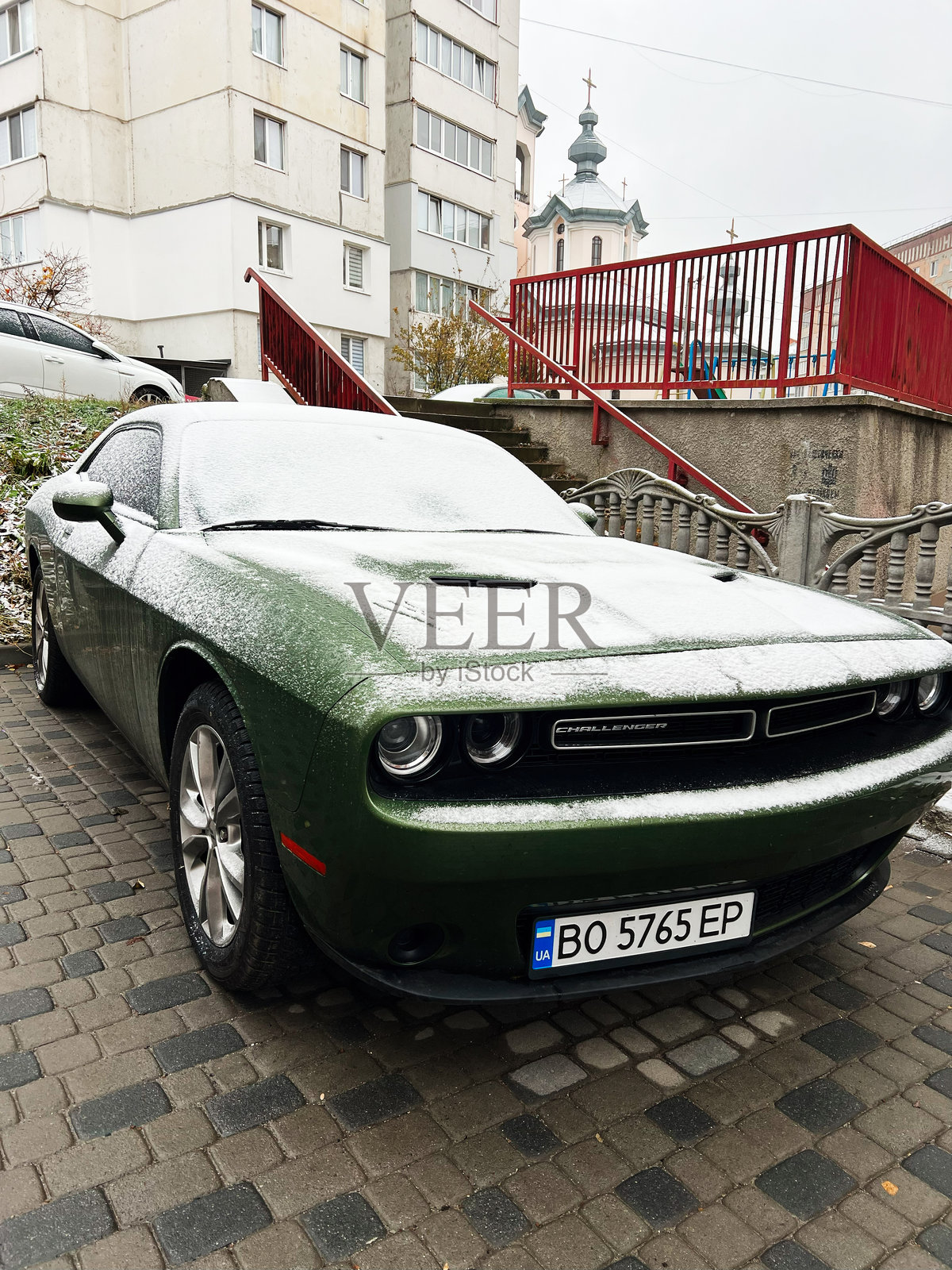 被雪覆盖的绿色道奇挑战者跑车，停靠在城市建筑附近照片摄影图片