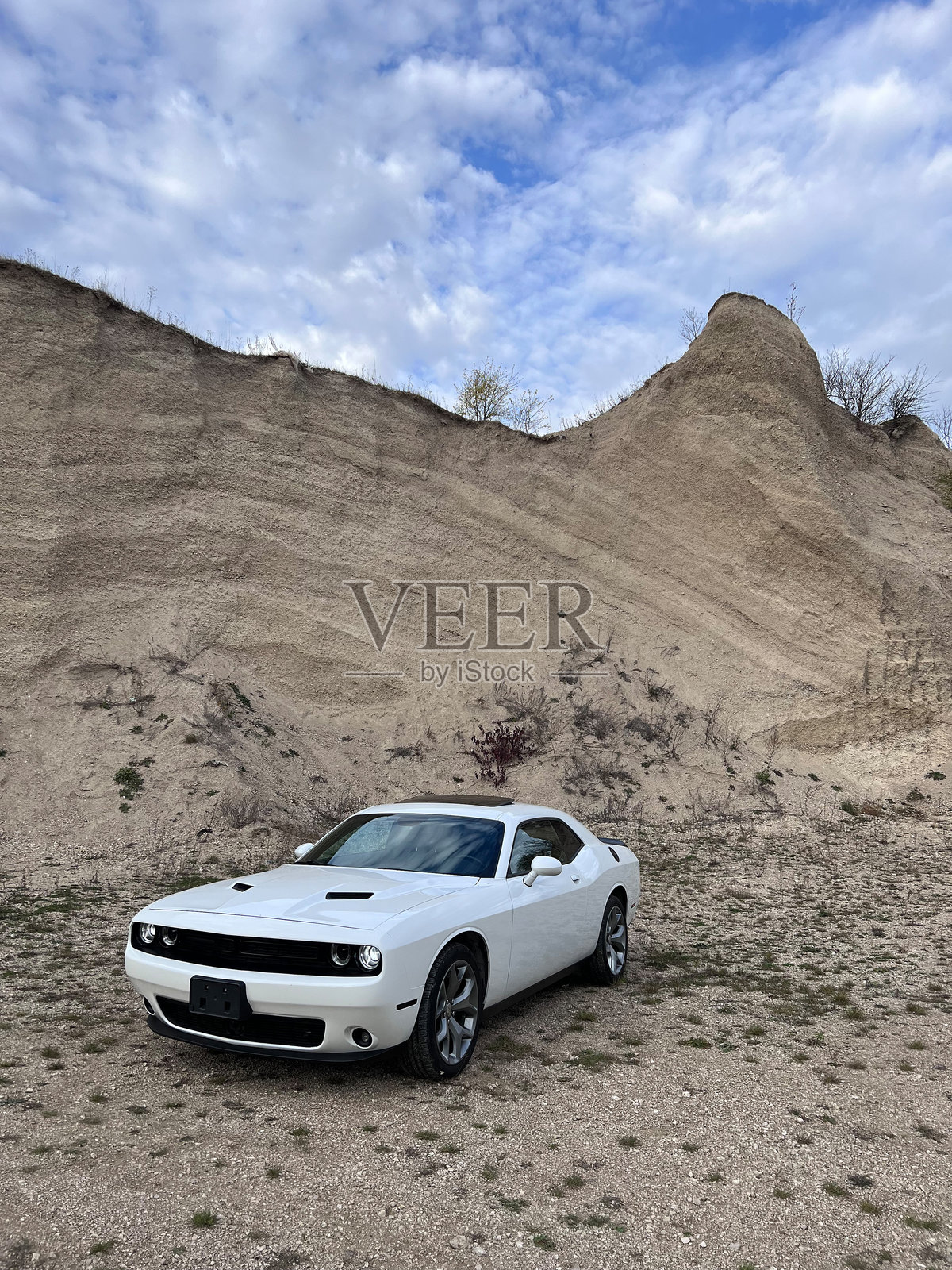 白色道奇挑战者汽车停在多云天气下的岩石山丘前照片摄影图片