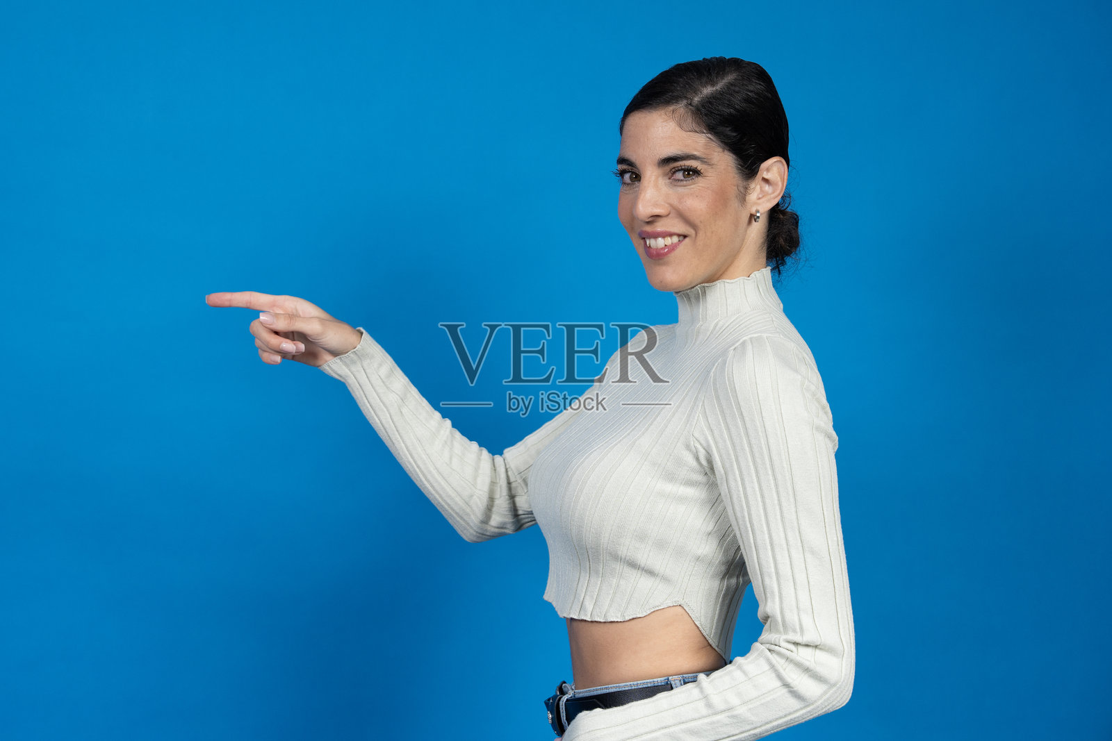 微笑的女性用手指指向蓝色背景上的某物照片摄影图片