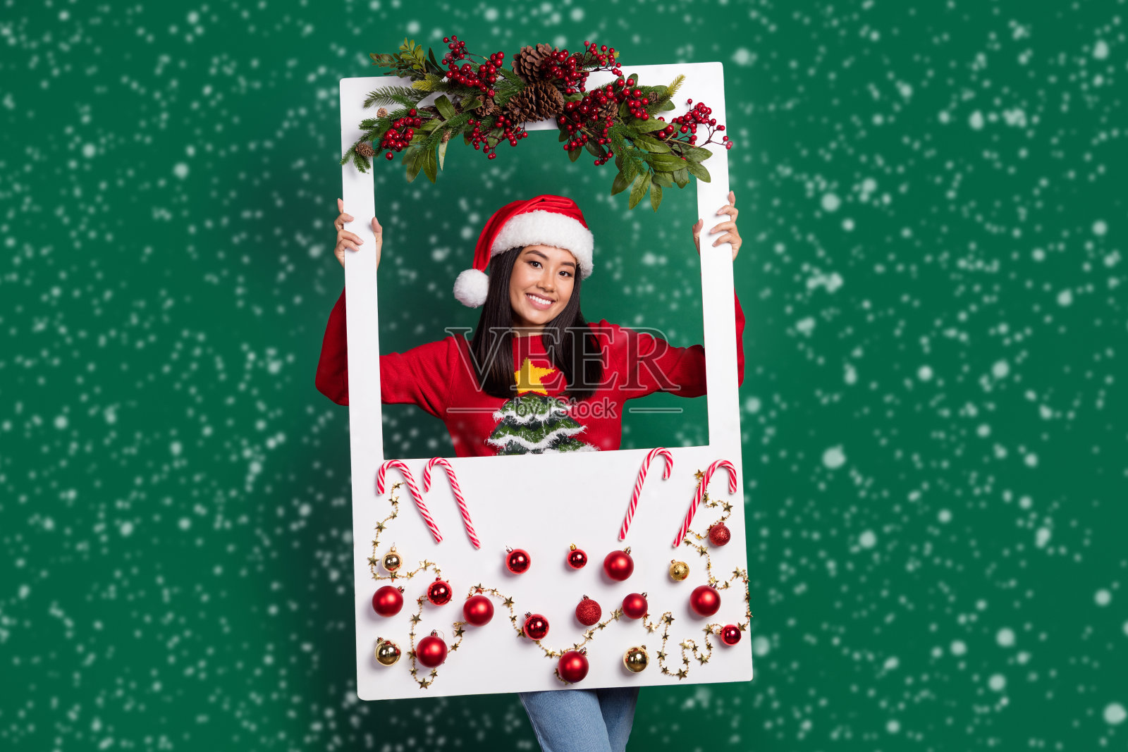 心情愉悦的满意女性肖像，长发披肩，穿着红色毛衣，手持圣诞窗框，背景为绿色。照片摄影图片