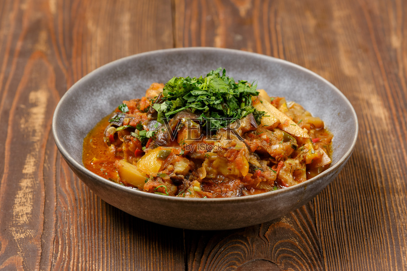 丰盛的蔬菜炖菜盛在质朴的碗中，点缀着新鲜的香草，摆放在木桌上。照片摄影图片