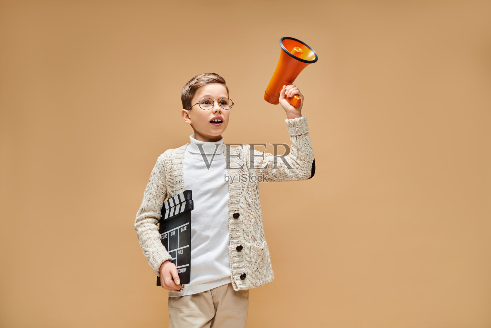 可爱的小男孩穿着创意服装，手持扩音器和电影拍板，置身于愉快的环境中照片摄影图片