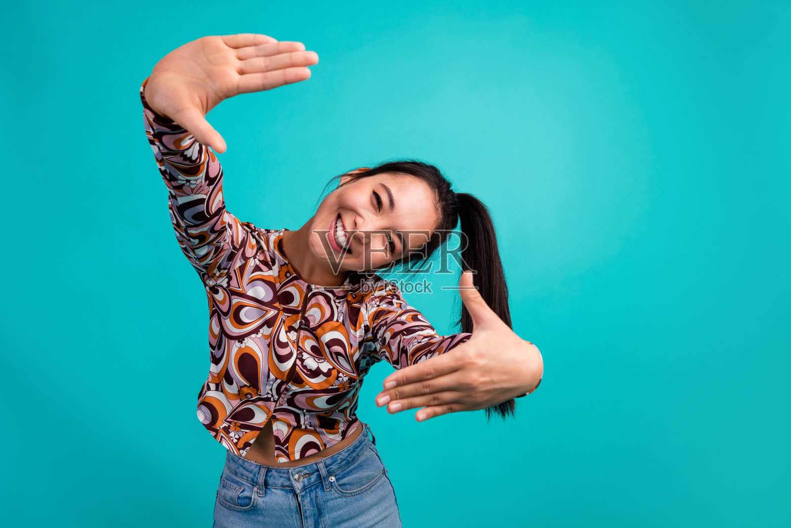 穿着时尚多彩衣服的迷人年轻女性手持照片框的肖像，背景为青色。照片摄影图片