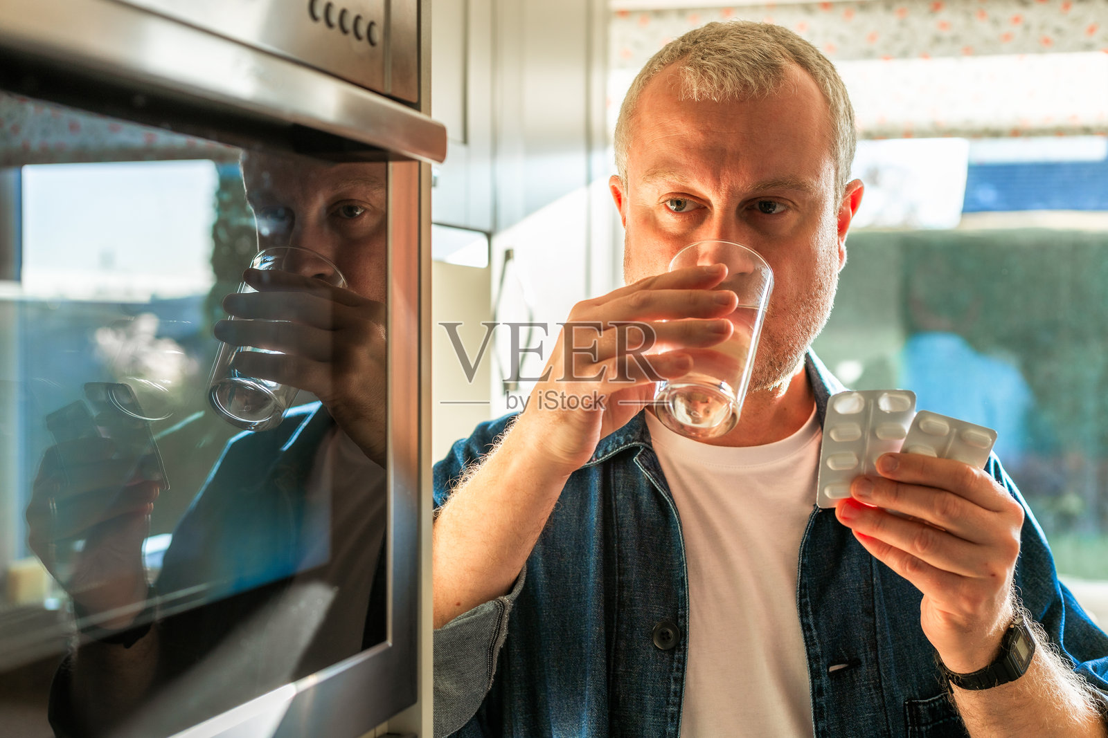 男人在厨房里喝水服用止痛药。照片摄影图片
