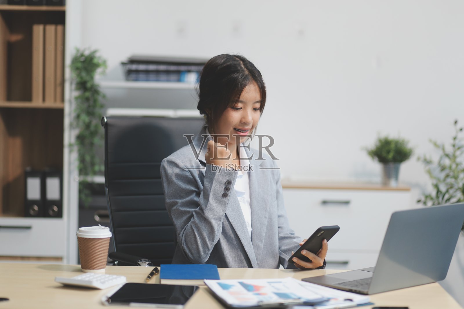 身穿正式西装的亚洲女商人在办公室愉快地使用智能手机工作。照片摄影图片