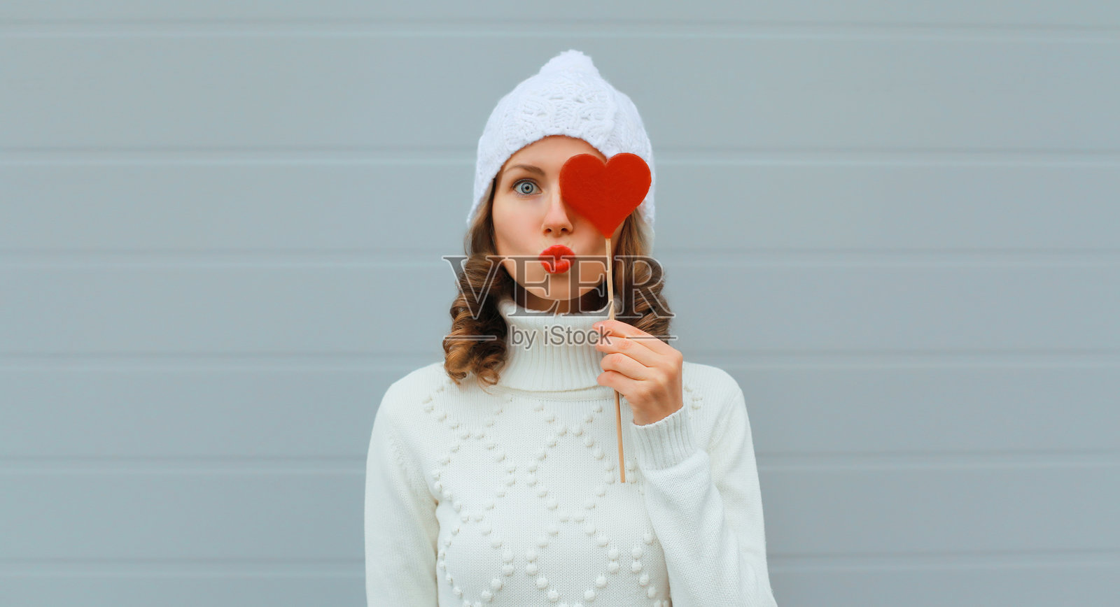 冬季圣诞节美丽快乐的年轻女性，戴着白色帽子，吹着吻，手里拿着棒棒糖。照片摄影图片