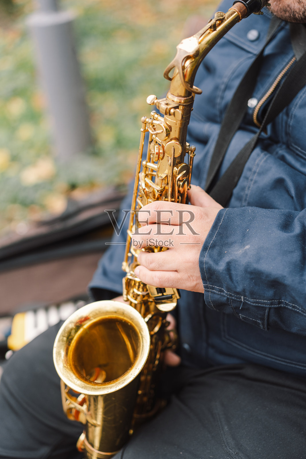 一位萨克斯演奏家在秋天的宁静公园里坐在长椅上演奏。照片摄影图片