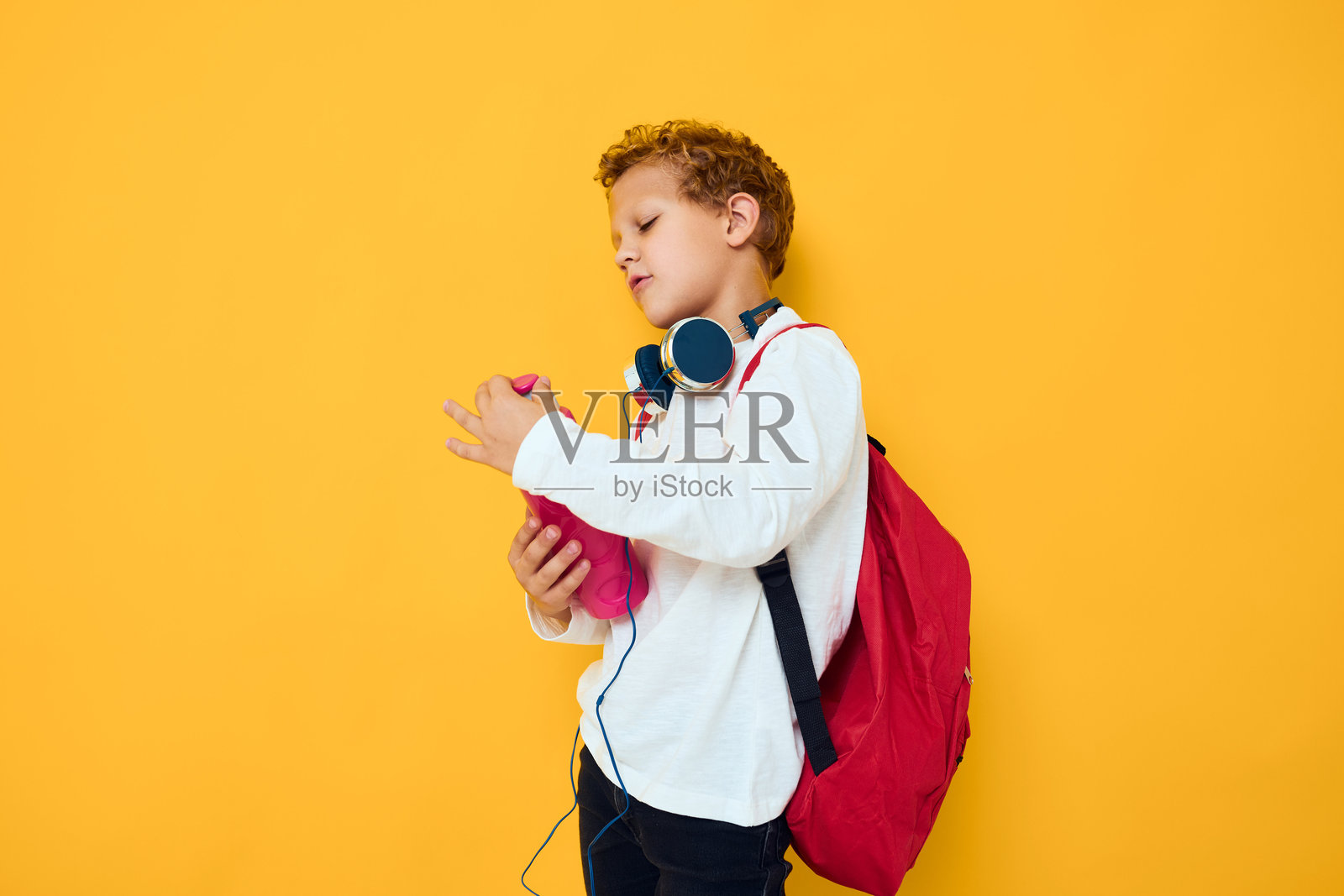 时尚男孩戴着耳机，手里拿着水瓶，背景为黄色。照片摄影图片